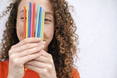 Smiling woman holding colored pencils in front of face - AMWF00981