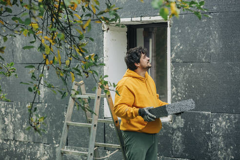 Man holding polystyrene looking at wall of house - VSNF00095