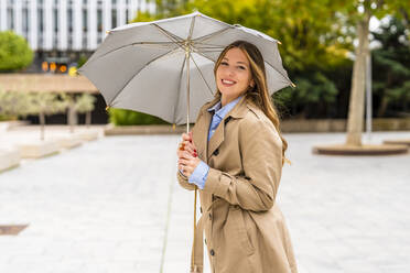 Glückliche Geschäftsfrau mit Regenschirm auf dem Fußweg - DLTSF03373