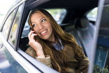 Lächelnde Geschäftsfrau, die im Auto mit einem Mobiltelefon spricht - DLTSF03391