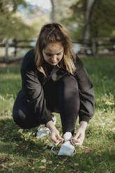 Young woman tying shoe lace in park - JBUF00092