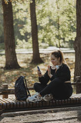 Smiling woman having video call through smart phone on bench in park - JBUF00102