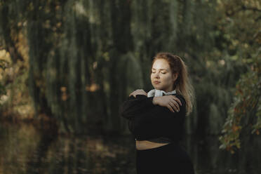 Woman with eyes closed hugging self in park - JBUF00103