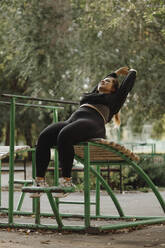 Smiling overweight woman doing stretching exercise at outdoor gym - JBUF00106