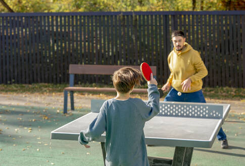 Sohn und Vater spielen Tischtennis an einem sonnigen Tag - ANAF00473