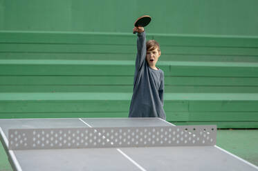 Boy holding table tennis racket screaming in front of green wall - ANAF00476