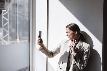 Geschäftsfrau gestikuliert OK-Zeichen und nimmt Selfie durch Handy im Büro - JOSEF14676