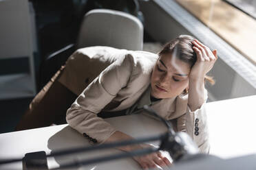 Traurige Geschäftsfrau, die sich im Büro auf einen Tisch stützt, gesehen durch Glas - JOSEF14687