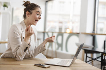 Businesswoman looking at laptop screaming with clenched fists in office - JOSEF14712