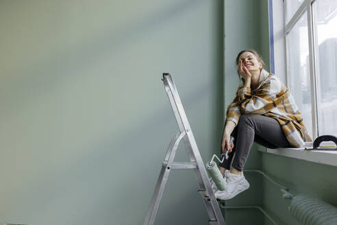 Smiling woman with hand on chin holding paint roller at home - VIVF00134