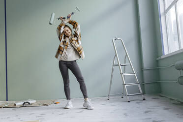 Smiling young woman dancing with work tools at home - VIVF00138