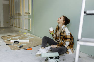 Junge Frau mit Einweg-Kaffeebecher lachend in Wohnung - VIVF00141