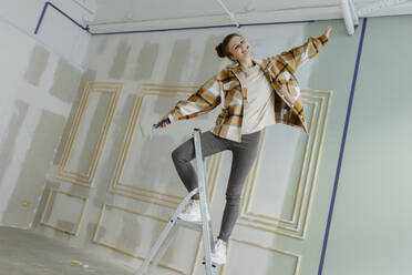 Happy woman dancing with arms outstretched on ladder at home - VIVF00144