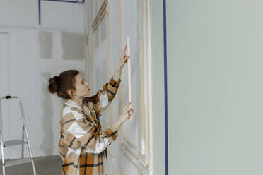 Young woman sticking wood on wall at home - VIVF00148