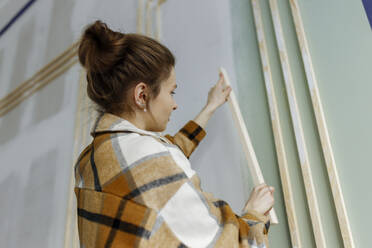 Junge Frau bei der Arbeit mit einem Holzstab in einer Wohnung - VIVF00150