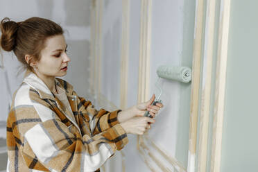 Young woman applying paint on wall renovating home - VIVF00152