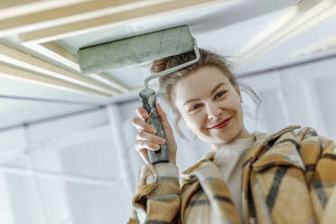 Lächelnde junge Frau mit Farbrolle beim Renovieren ihres Hauses - VIVF00153