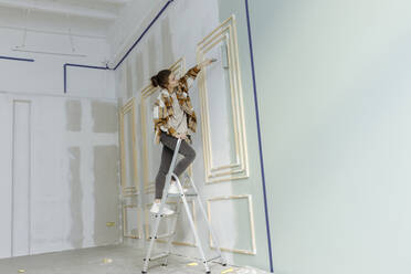 Young woman painting with paint roller on wall at home - VIVF00154