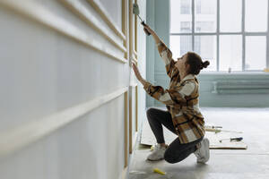 Junge Frau trägt Farbe auf eine Wand in einer Wohnung auf - VIVF00160