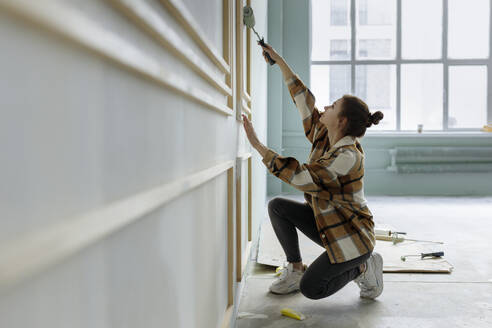 Young woman applying paint on wall in apartment - VIVF00160