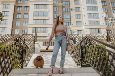 Smiling woman with dog moving down on steps in front of building - MDOF00178