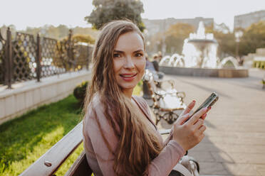 Glückliche Frau hält Smartphone auf Bank - MDOF00184