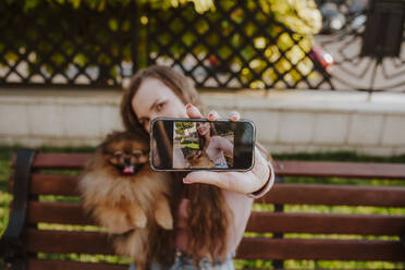 Frau zeigt ihr Selfie mit Hund auf dem Mobiltelefon - MDOF00186