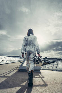 Astronaut wearing space suit holding helmet walking on footpath - DAMF01111