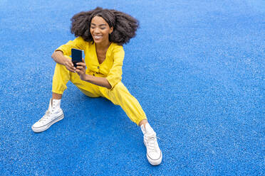 Glückliche junge Frau mit Smartphone auf blauem Basketballplatz - DLTSF03409
