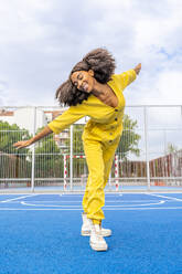 Happy woman with Afro hairstyle dancing on basketball court - DLTSF03415