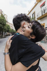 Happy young woman embracing boyfriend on footpath - JRVF03174