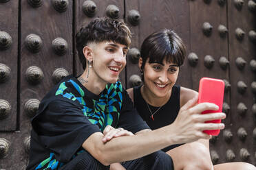 Happy young couple having video call through smart phone in front of door - JRVF03186