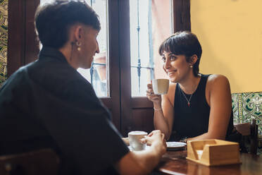 Glückliche junge Frau mit Kaffeetasse im Gespräch mit ihrem Freund in einem Café - JRVF03192