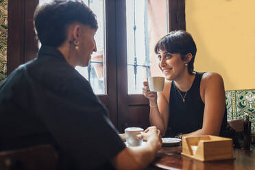 Happy young woman holding coffee cup talking with boyfriend in cafe - JRVF03192
