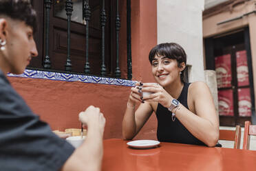 Lächelnde Frau mit Kaffeetasse, die mit ihrem Freund in einem Straßencafé sitzt - JRVF03196