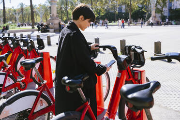 Frau, die an einer Parkstation über ihr Smartphone ein Fahrrad ausleiht - MMPF00501