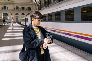 Frau prüft am Bahnhof die Zeit auf der Armbanduhr - MMPF00511