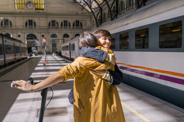 Glückliche Frau mit Roller, die einen Freund am Bahnhof umarmt - MMPF00512