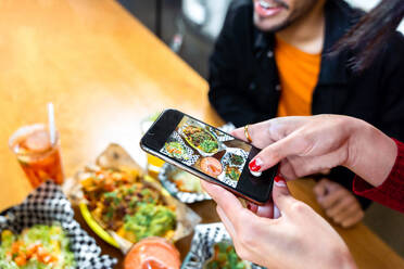 Anonyme Freunde fotografieren köstliche Speisen mit ihren Smartphones, während sie sich in einem Restaurant an einen Tisch setzen - ADSF40225