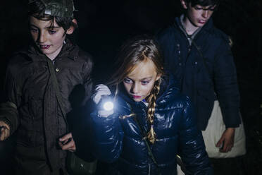 Group of three children camping and playing with torch lantern in the dark - ADSF40254