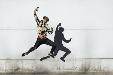 Black man jumping and taking selfie near wall - ADSF40273