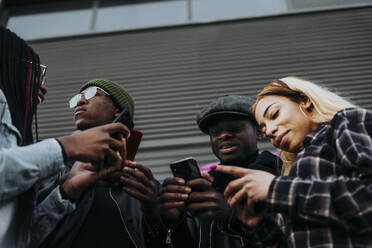 From below young African American people browsing modern smartphones while standing on city street together - ADSF40282