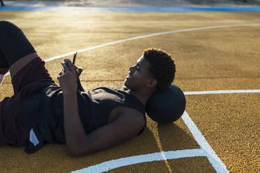 Seitenansicht eines afroamerikanischen Sportlers in Uniform, der auf ein Handy schaut - ADSF40299