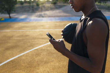 Seitenansicht eines afroamerikanischen Sportlers in Uniform, der auf ein Handy schaut - ADSF40300