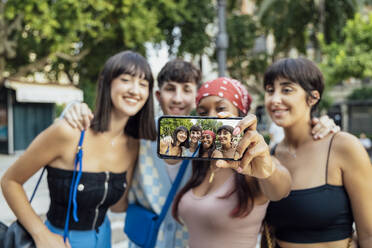 Frau zeigt ihr Selfie auf dem Handy mit Freunden im Park - JRVF03230