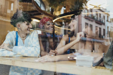 Happy friends talking in cafe seen through glass - JRVF03249