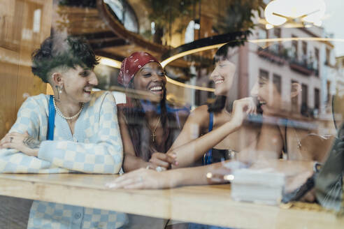 Glückliche Freunde unterhalten sich in einem Café durch Glas gesehen - JRVF03249