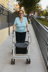 Smiling senior woman with walker on footpath - EGHF00620