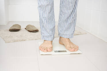 Man standing on weight scale in bathroom at home - EYAF02318