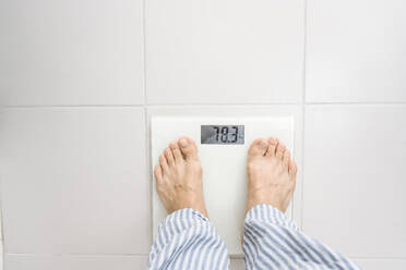 Man standing on weight scale at home - EYAF02319